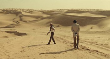 Movie still from “The Mattei Affair” (1972), directed by Francesco Rosi – Two people walking in the sand in the desert; Extreme Wide shot, High angle