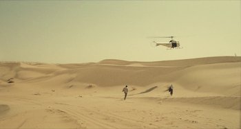 Movie still from “The Mattei Affair” (1972), directed by Francesco Rosi – Two people running in the desert while a helicopter hovers overhead; Extreme Wide shot, High angle