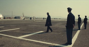 Movie still from “The Mattei Affair” (1972), directed by Francesco Rosi – Two men are walking across a runway in front of an airplane; Wide shot, Low angle