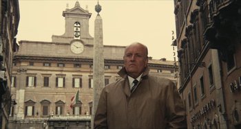 Movie still from “The Mattei Affair” (1972), directed by Francesco Rosi – An older man in a trench coat standing in front of a building; Medium shot, Low angle