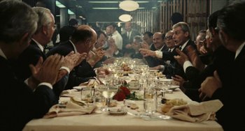 Movie still from “The Mattei Affair” (1972), directed by Francesco Rosi – A group of people sitting at a table eating food; Wide shot, High angle