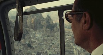 Movie still from “The Mattei Affair” (1972), directed by Francesco Rosi – A man looking out of a helicopter window at a city; Close Up shot, High angle