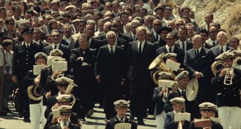 Movie still from “The Mattei Affair” (1972), directed by Francesco Rosi – A large group of men in suits marching down a street; Wide shot, High angle