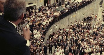 Movie still from “The Mattei Affair” (1972), directed by Francesco Rosi – A crowd of people in suits and ties standing on a sidewalk; Extreme Wide shot, Overhead angle