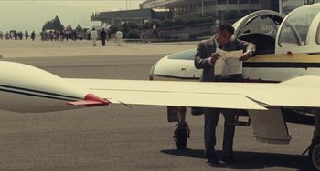 Movie still from “The Mattei Affair” (1972), directed by Francesco Rosi – A man standing next to an airplane on a runway; Wide shot, High angle