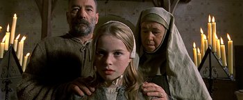 Movie still from “The Messenger: The Story of Joan of Arc” (1999), directed by Luc Besson – A young girl with her hands on the shoulders of an older woman and an older man; Close Up shot, Low angle