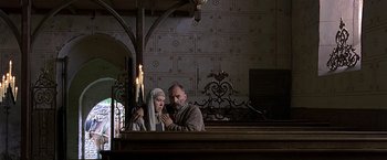 Movie still from “The Messenger: The Story of Joan of Arc” (1999), directed by Luc Besson – A man and a woman are standing in front of candles; Wide shot, Low angle