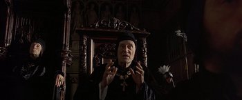 Movie still from “The Messenger: The Story of Joan of Arc” (1999), directed by Luc Besson – An old man wearing a black hat and a black robe; Medium shot, High angle
