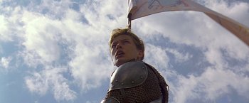 Movie still from “The Messenger: The Story of Joan of Arc” (1999), directed by Luc Besson – A man wearing a suit of armor and holding a flag; Close Up shot, Low angle