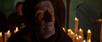 Movie still from “The Messenger: The Story of Joan of Arc” (1999), directed by Luc Besson – An old man wearing a black robe and a black hood; Close Up shot, Over the shoulder angle