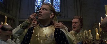Movie still from “The Messenger: The Story of Joan of Arc” (1999), directed by Luc Besson – A man in a suit of armor is putting on a crown while a man in a suit of armor looks on; Close Up shot, Low angle