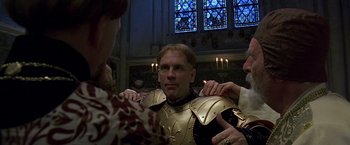 Movie still from “The Messenger: The Story of Joan of Arc” (1999), directed by Luc Besson – A man wearing a golden armor is being held by two other men; Close Up shot, Low angle