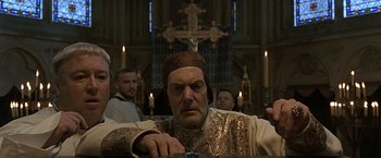 Movie still from “The Messenger: The Story of Joan of Arc” (1999), directed by Luc Besson – A man sitting in front of a cross in a church; Medium shot, Low angle
