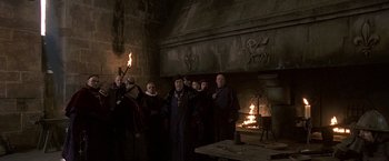 Movie still from “The Messenger: The Story of Joan of Arc” (1999), directed by Luc Besson – A group of people standing in front of a fireplace; Wide shot, High angle