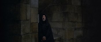 Movie still from “The Messenger: The Story of Joan of Arc” (1999), directed by Luc Besson – A man dressed in black standing next to a stone wall; Medium shot, High angle