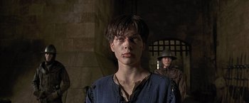 Movie still from “The Messenger: The Story of Joan of Arc” (1999), directed by Luc Besson – A young man standing in front of a brick wall; Close Up shot, Low angle