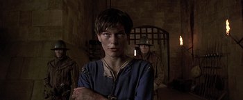 Movie still from “The Messenger: The Story of Joan of Arc” (1999), directed by Luc Besson – A man in a blue shirt standing next to another man in a brown hat; Close Up shot, Over the shoulder angle