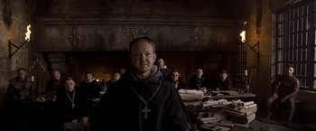 Movie still from “The Messenger: The Story of Joan of Arc” (1999), directed by Luc Besson – A man wearing a priest's outfit standing in front of a group of people; Medium shot, Low angle