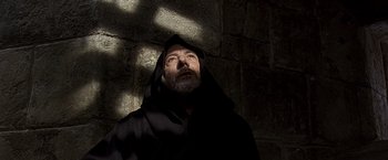 Movie still from “The Messenger: The Story of Joan of Arc” (1999), directed by Luc Besson – A man with a beard and a black robe is looking up; Close Up shot, Low angle