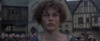 Movie still from “The Messenger: The Story of Joan of Arc” (1999), directed by Luc Besson – A young man with blue eyes is standing in front of a building; Close Up shot, Low angle