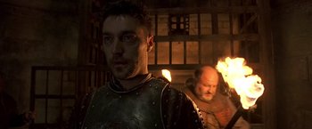 Movie still from “The Messenger: The Story of Joan of Arc” (1999), directed by Luc Besson – A man in a leather jacket standing next to another man in a suit of armor; Close Up shot, Low angle