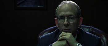 Movie still from “The Mexican” (2001), directed by Gore Verbinski – A man with glasses and a ring is sitting in a chair; Close Up shot, Over the shoulder angle
