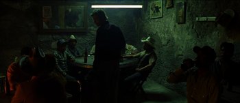 Movie still from “The Mexican” (2001), directed by Gore Verbinski – A group of people sitting at a table in a dark room; Wide shot, Low angle