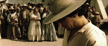 Movie still from “The Mexican” (2001), directed by Gore Verbinski – A group of people standing around a man wearing a hat; Medium shot, Low angle