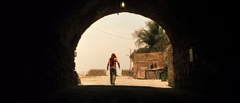 Movie still from “The Mexican” (2001), directed by Gore Verbinski – A person walking through an archway on a dirt road; Wide shot, Low angle