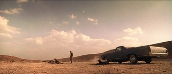 Movie still from “The Mexican” (2001), directed by Gore Verbinski – A man standing next to an old car on a dirt road; Extreme Wide shot, Low angle