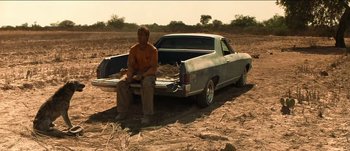 Movie still from “The Mexican” (2001), directed by Gore Verbinski – A man sitting on the back of a truck in the middle of a field; Wide shot, Low angle