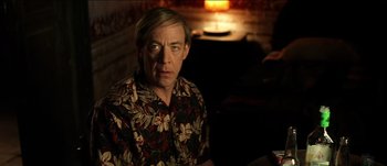 Movie still from “The Mexican” (2001), directed by Gore Verbinski – A man in a floral shirt sitting in a room; Medium shot, Low angle