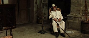 Movie still from “The Mexican” (2001), directed by Gore Verbinski – An older man sitting in a rocking chair with a cane; Wide shot, Low angle