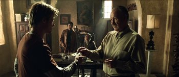 Movie still from “The Mexican” (2001), directed by Gore Verbinski – A man is handing a card to another man in a room; Medium shot, Over the shoulder angle