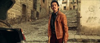 Movie still from “The Mexican” (2001), directed by Gore Verbinski – A man in a brown leather jacket holding a wooden stick; Medium shot, Low angle