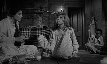 Movie still from “The Miracle Worker” (1962), directed by Arthur Penn – A little girl sitting on the floor next to a glass of milk; Medium shot, Over the shoulder angle