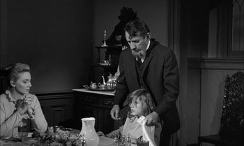 Movie still from “The Miracle Worker” (1962), directed by Arthur Penn – A man and a little girl are standing at a dinner table; Medium shot, Over the shoulder angle