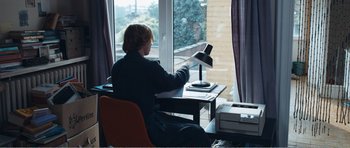 Movie still from “The Misfortunates” (2009), directed by Felix van Groeningen – A man sitting at a desk in front of a window; Medium shot, Over the shoulder angle