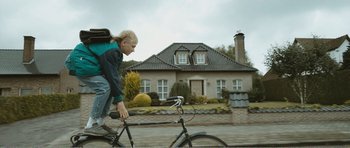 Movie still from “The Misfortunates” (2009), directed by Felix van Groeningen – A person riding a bike in front of a house; Wide shot, Low angle