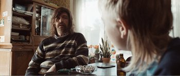 Movie still from “The Misfortunates” (2009), directed by Felix van Groeningen – A man sitting at a table with a bottle of medicine; Medium shot, Over the shoulder angle