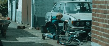 Movie still from “The Misfortunates” (2009), directed by Felix van Groeningen – A woman fixing a bicycle tire on the side of the road; Wide shot, Low angle