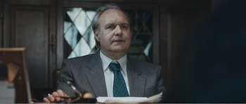 Movie still from “The Misfortunates” (2009), directed by Felix van Groeningen – A man in a suit and tie sitting at a table; Close Up shot, Over the shoulder angle