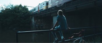 Movie still from “The Misfortunates” (2009), directed by Felix van Groeningen – A man sitting on a rail next to a bridge; Wide shot, Low angle