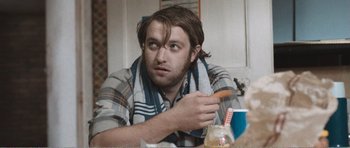 Movie still from “The Misfortunates” (2009), directed by Felix van Groeningen – A man sitting at a table with a hot dog in his hand; Close Up shot, Over the shoulder angle