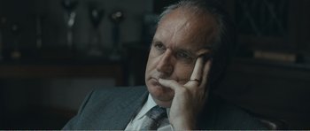 Movie still from “The Misfortunates” (2009), directed by Felix van Groeningen – An older man wearing a suit and tie with his hand under his chin; Close Up shot, Over the shoulder angle