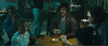 Movie still from “The Misfortunates” (2009), directed by Felix van Groeningen – A man sitting at a table with two beers and a cake; Medium shot, Over the shoulder angle