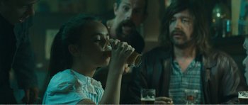 Movie still from “The Misfortunates” (2009), directed by Felix van Groeningen – A woman drinking a beer while sitting at a table; Medium shot, Over the shoulder angle