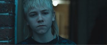 Movie still from “The Misfortunates” (2009), directed by Felix van Groeningen – A boy with long blonde hair is looking at the camera; Close Up shot, Over the shoulder angle