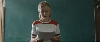 Movie still from “The Misfortunates” (2009), directed by Felix van Groeningen – A young boy is reading a book in front of a chalkboard; Medium shot, Over the shoulder angle
