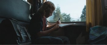 Movie still from “The Misfortunates” (2009), directed by Felix van Groeningen – A person sitting on a train writing on a piece of paper; Medium shot, Over the shoulder angle